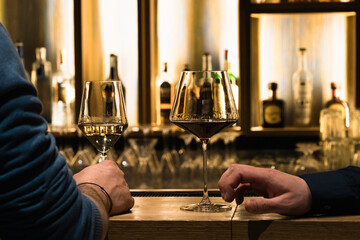 Male hand holding a glass of wine, blurred restaurant detail in the background.