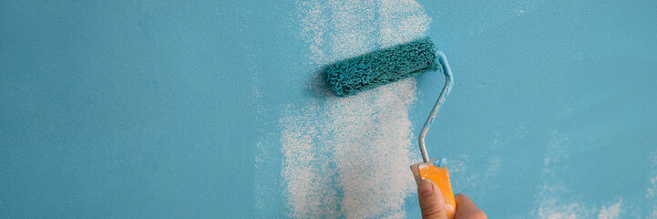 Decorator hand painting walls in blue color with roller
