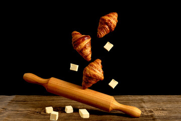 croissants with pieces of butter and rolling pin on black and wooden background
