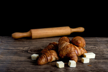 croissants with pieces of butter and rolling pin on black and wooden background