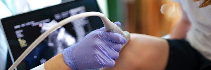 Specialist making ultrasound diagnostics of knee joint of little child