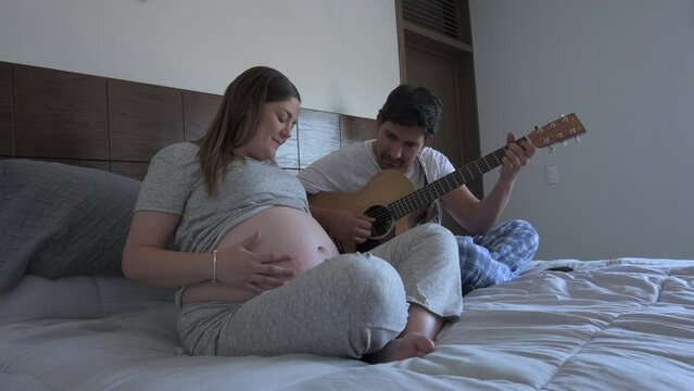 happy husband plays the guitar for his pregnant wife and sings to the tummy