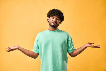 Emotion of choice, doubt. A handsome Indian man stands on a yellow background and spreads his...