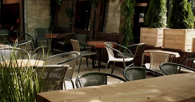 Wooden Tables with black modern charis in cafe on the street. Empty cafe in the summer morning. Modern outdoor cafe. Street cafe. Modern Terrace. Empty restaurant.