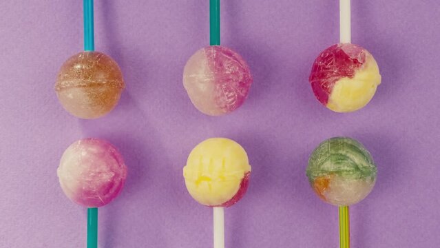 Sweet lollipops with glitter sprinkles on color purple background zoom frame. Bright texture sugar candies close up top view. Composition of favorite children's summer sweets. Studio shot for shop