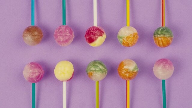 Sweet lollipops appear on color purple background. Bright texture sugar candies close up top view. Composition of favorite children's summer sweets. Studio shot for shop, supermarket, confectionery 