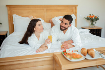 Couple Enjoying Breakfast In Bed, Drinking Fresh Juice In Bedroom
