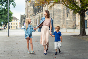Young adult beautiful mom enjoy having fun walking with two kids in european city street at summer...
