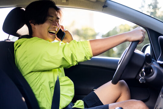 A young Korean man is sending talking on his mobile phone while driving a car. Concept of danger on the road, recklessness with the steering wheel,use the phone while driving.