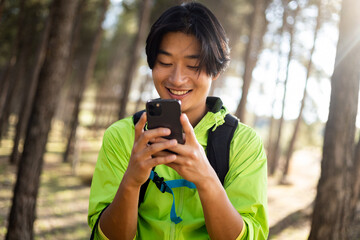 A young Korean man is hiking up the mountain while chatting on his mobile phone. Concept of coverage in the field, use the mobile in the mountains, send messages from afar.