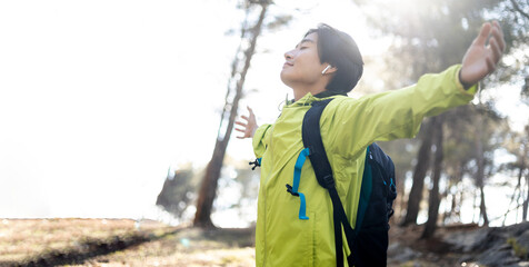 A young Korean man is posing with open arms in the middle of the mountain with his eyes closed....