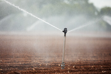 Agricultural irrigation equipment spraying water on dry filed. Themes drought, environment and agriculture..