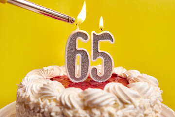 A candle in the form of the number 65, stuck in a festive cake, is lit. Celebrating a birthday or a...