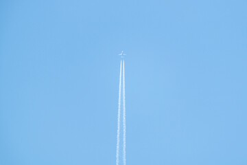 A plane soars high in a clear blue sky, leaving behind a trail of white smoke. Ample copy space allows for creative customisation. Travel concept