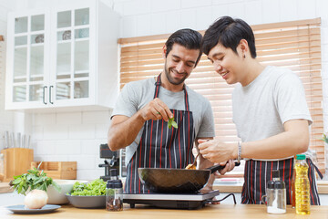 Fototapeta na wymiar LGBTQ+ gay bisexual cooking their meal together in the kitchen, LGBTQ gay couple making a spaghetti. A different ethnicity handsome gay couple enjoy cooking a spaghetti together in kitchen.