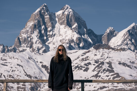 Portrait of stylish man wearing round sunglasses in front of snowy mountain peaks on vacation