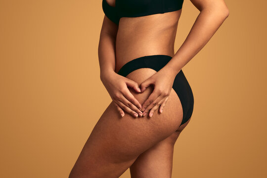 Crop woman showing heart gesture on hip in studio