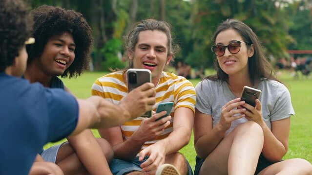 A Group of Multiethnic Young friends sitted in the Park, Talking and Laughing. Diverse Friends watching funny videos on mobile smartphone
