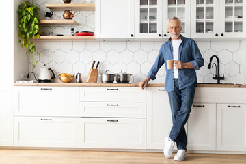 Portrait Of Happy Senior Man With Cup Of Coffee Posing In Kitchen