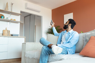 Fototapeta premium Relaxed Indian Man Turning On Air Conditioner Sitting At Home