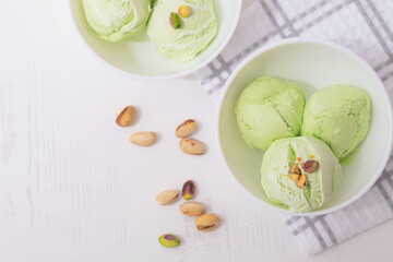 Pistachio homemade ice cream decorated with nuts in white bowls on a white kitchen table, copy space. Summer cooling desserts