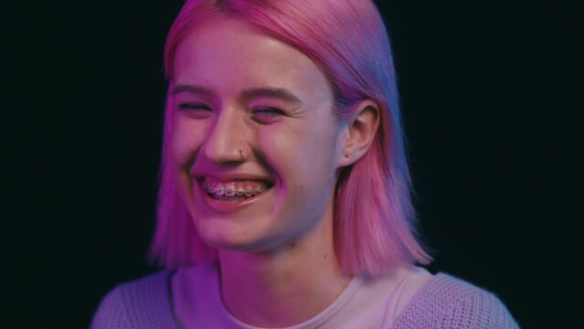 Cheerful young woman with braces smiling sincerely on black background, mood
