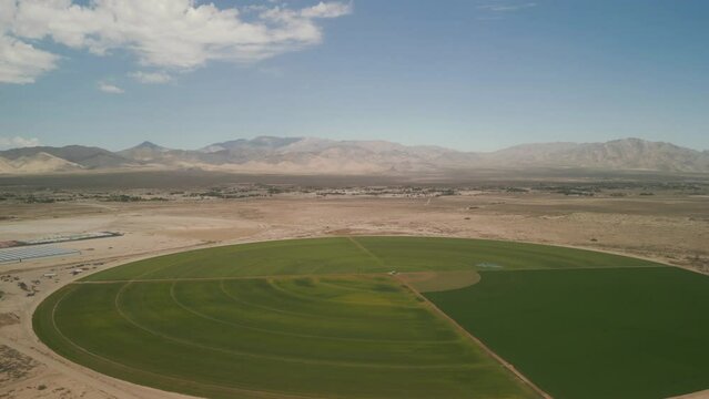 Aerial drone footage of a circle with green meadows in a desert in blue sky background