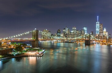 Naklejka na ściany i meble Scenic shot of the city of New York and Brooklyn bridge at night with bright beautiful city lights