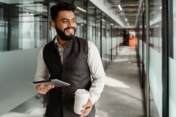 Young indian man in suit using tablet computer in office corridor