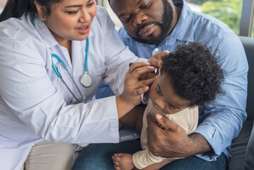 an Asian female doctor doing a preliminary examination in the ear of a 10-month-old Nigerian baby boy, whose father is holding him. to health care baby and ear infection concept.