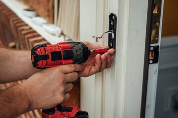 A man carpenter fixing a door knob with a drill