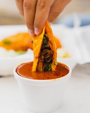 Vertical closeup of a birria taco being dipped into consome