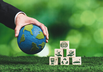 Businessman hand holding wooden cube with eco symbol and paper globe on fertile soil background....