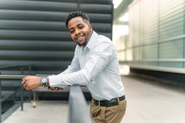 In a moment of respite, a charming Black businessman leans against a railing, absorbed in his phone...