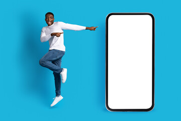 Fototapeta na wymiar Positive happy black guy jumping next to big phone, mockup