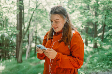 Young woman listening music on headphones resting after a walk in the forest, carrying a backpack in the forest on sunset light in the summer season. High quality photo