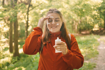 Young woman in a orange sport clothes applying sunscreen lotion while traveling in the mountains....