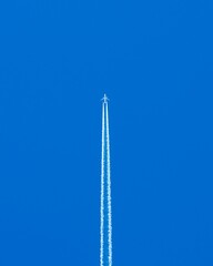 Vertical shot of an airplane flying in blue sky leaving smoke on its trace