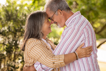 Cheerful european mature couple hugging, want to kiss, enjoy spare time together in park at summer weekend