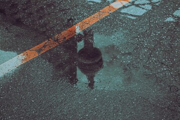 Dark reflection of the Olympiaturum tower in a puddle of water on the road