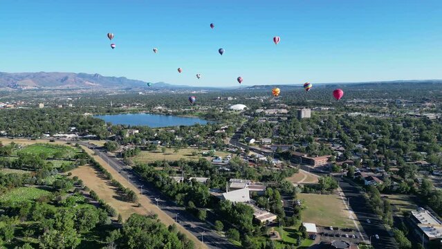 Aerial footage of colorful hot air balloons above the houses, trees, lakes, roads, and cars