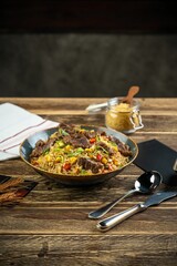 Fried rice dish with beef pieces and cutlery on a wooden table, vertical shot
