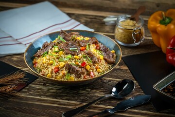 Closeup shot of Fried rice dish with beef pieces and cutlery on a wooden table