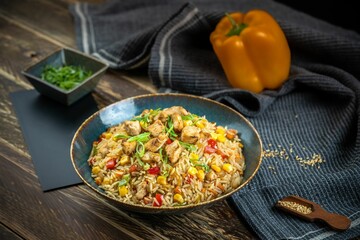Fried rice dish and small herb plate and yellow Bell pepper on a wooden table with gray cloth