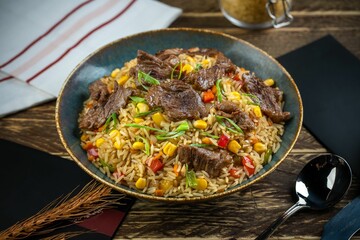 Fried rice dish with beef pieces and cutlery on a wooden table with blur gray cloth