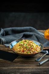 Fried rice dish with cutlery on a wooden table with gray cloth, vertical shot