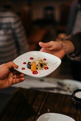 Vertical shot of a waiter serving a white plate of decorated dish to a person at a restaurant