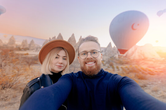 Couple lovers tourist making selfie photo in Cappadocia with colorful hot air balloon with sun light. Concept banner travel Turkey Goreme
