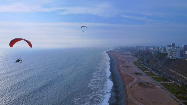 Aerial view of splashing waves on coastal beach with Paragliding sport in Lima