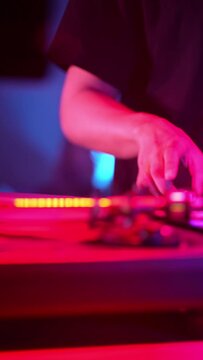 Vertical video, DJ mixes tracks on DJ console lit color music in nightclub party. Dj Mixer Controller Desk in Night Club Disco Party. Hands touching Buttons and Sliders Playing Electronic Music
